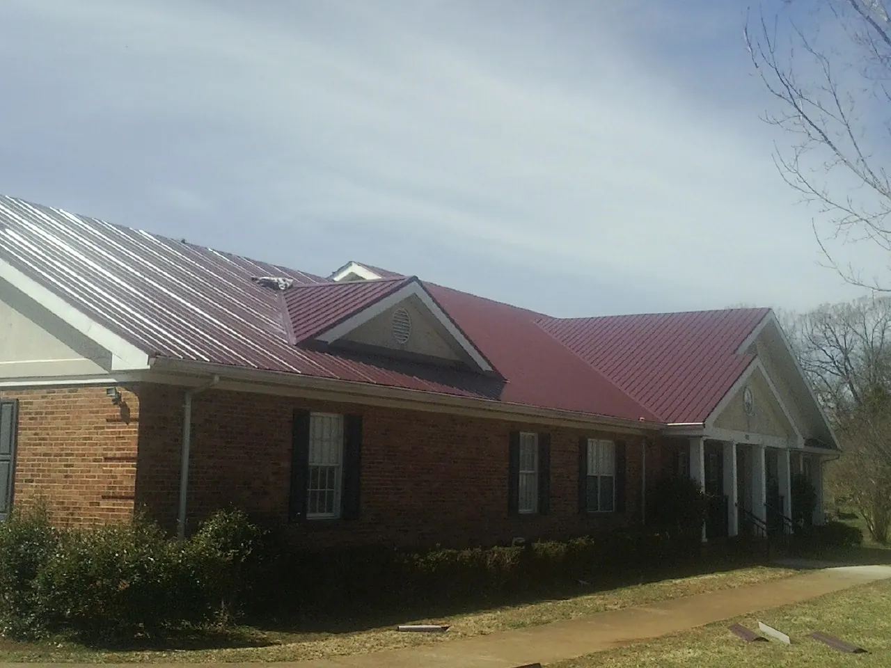 Red metal roof with gabled entries on a long brick building, from a Hail Damage Roof Repair job in Port Charlotte