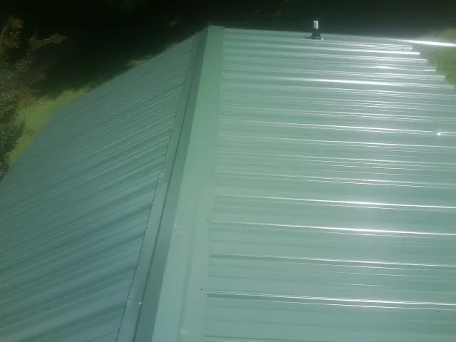 New green metal panels meeting at the ridge of a roof — Flat Roof Repair work by our crew in Port Charlotte