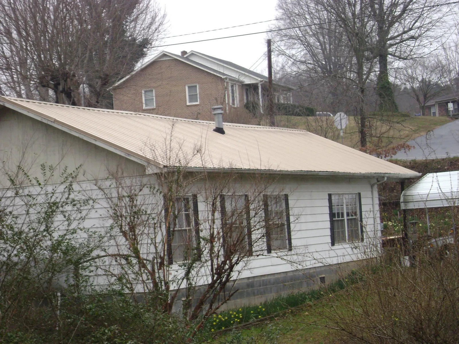 Tan metal roof on a white sided house set into a hillside — Commercial Roofing by Roofing Brothers in Port Charlotte